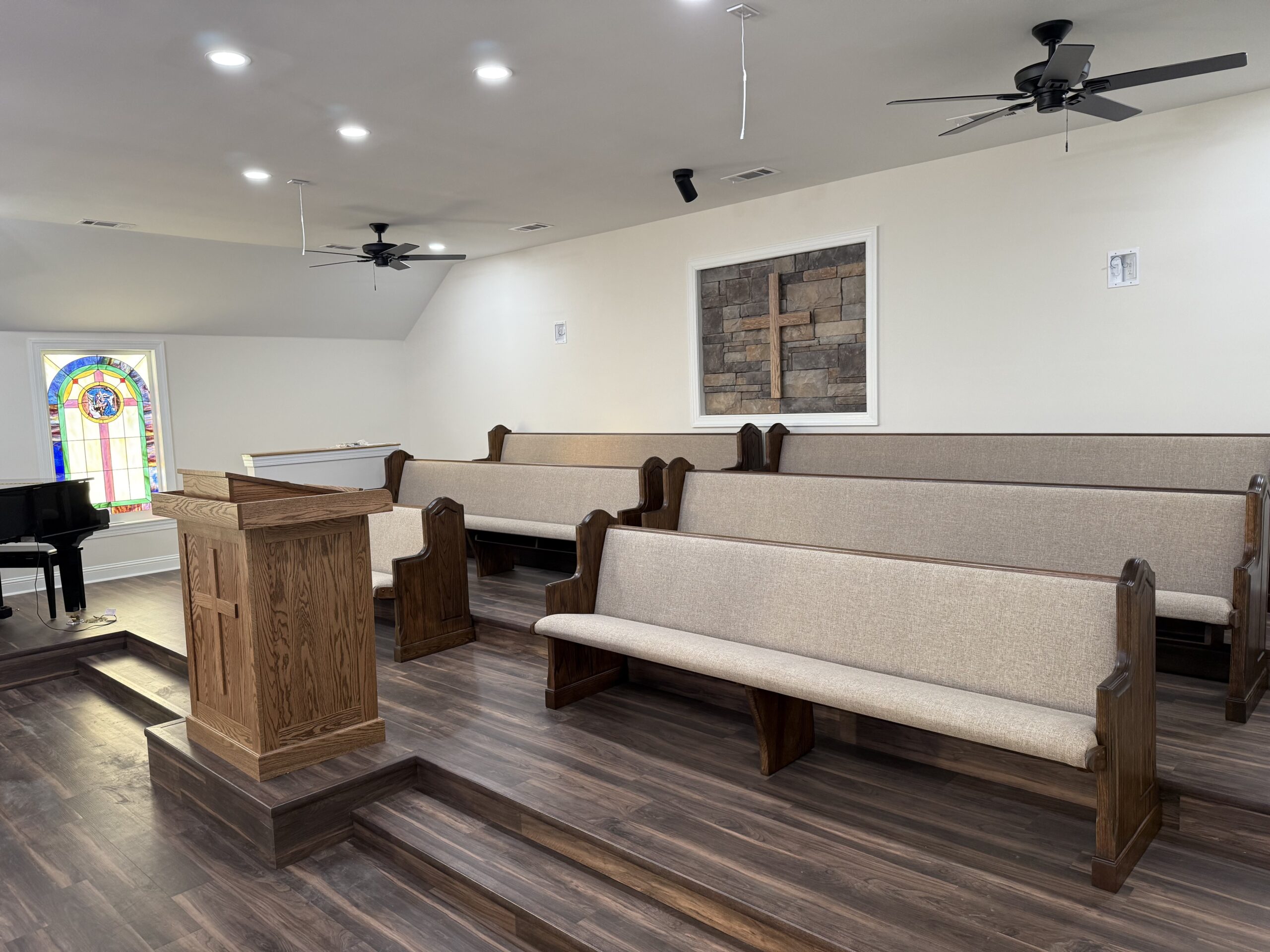 Restored church sanctuary with refinished wood-frame pews, wood floor, and stained glass window