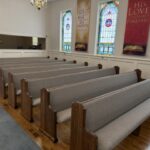 Restored oak church pews in rows down a historic sanctuary with stained-glass windows and refinished hardwood floors
