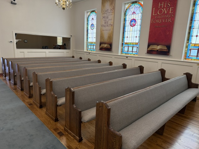 Restored oak church pews in rows down a historic sanctuary with stained-glass windows and refinished hardwood floors