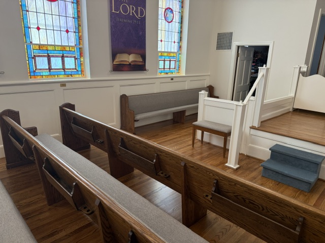 Restored church pews and platform steps with white railing and refinished hardwood flooring in an updated historic sanctuary